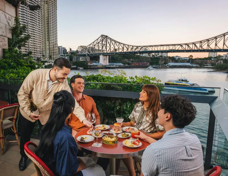 Friends eating and making a toast on a riverside terrace at sunset