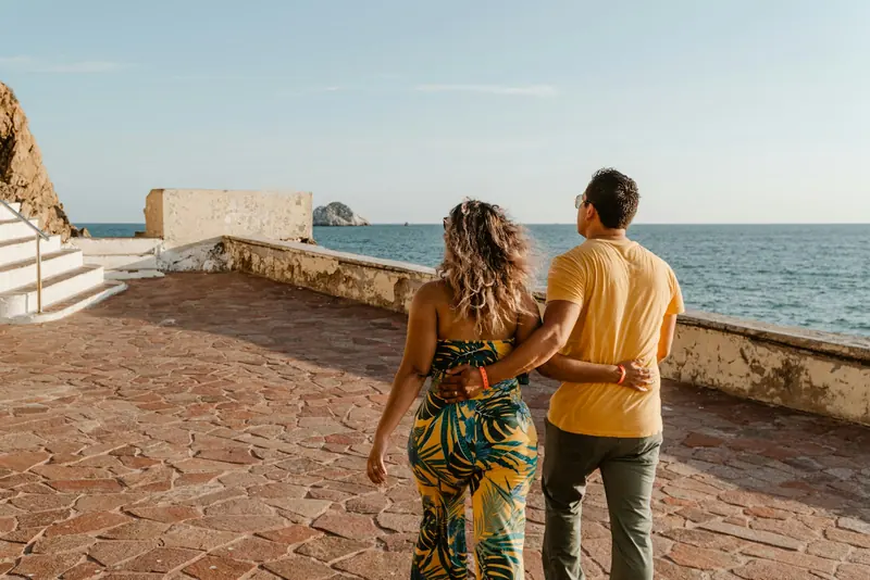 Parella passejant abraçada per un passeig marítim davant del mar