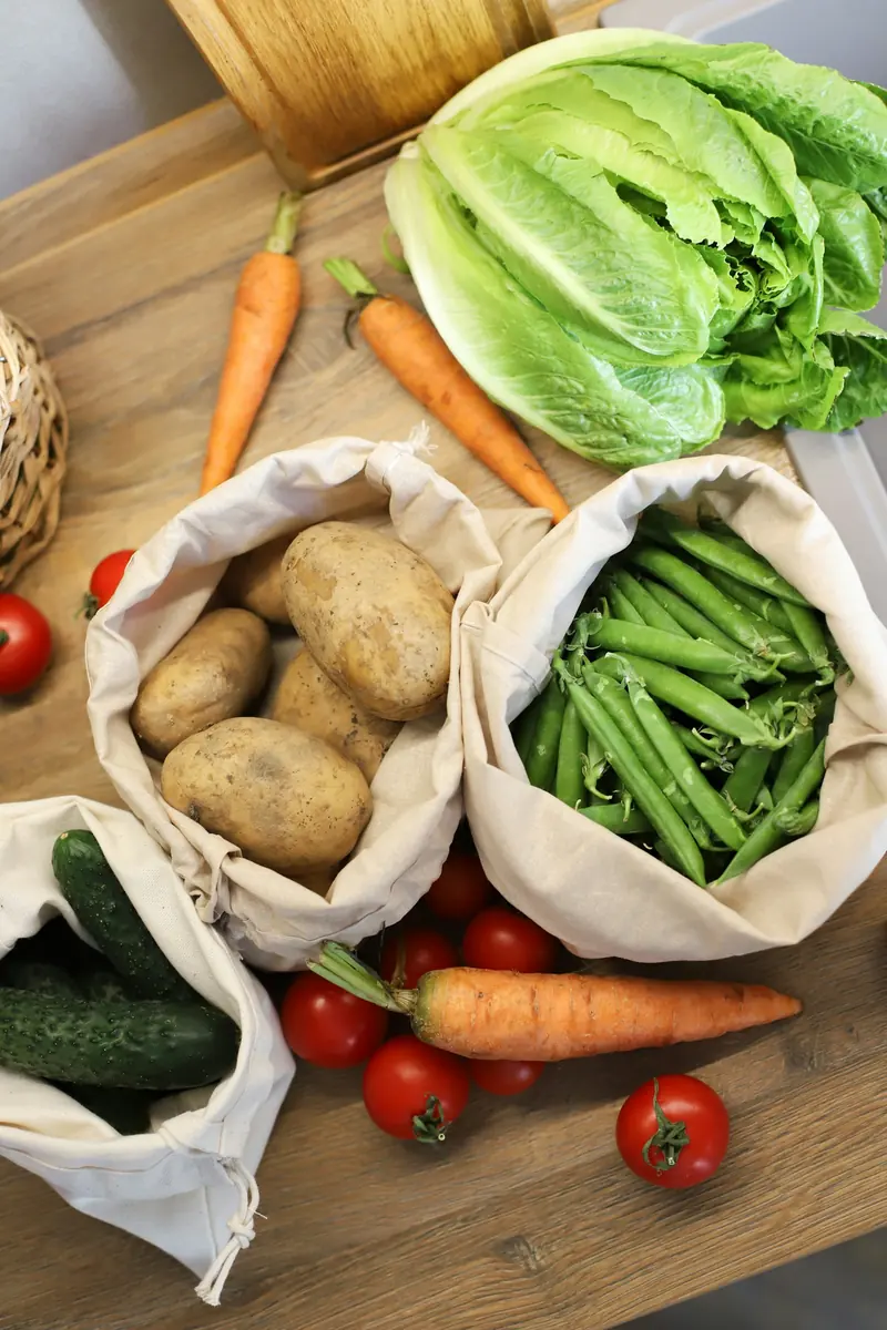 Cloth bags with potatoes, peas and cucumbers next to lettuce, carrots and tomatoes