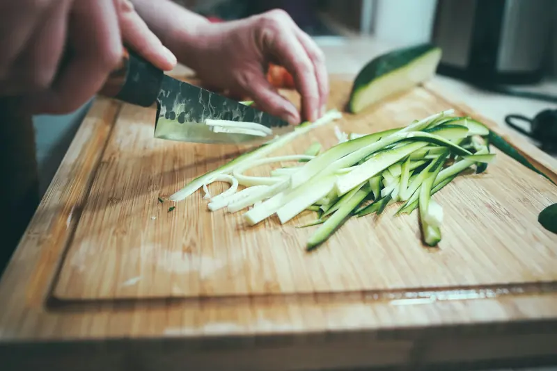 Manos cortando verduras en tiras con un cuchillo sobre una tabla de madera
