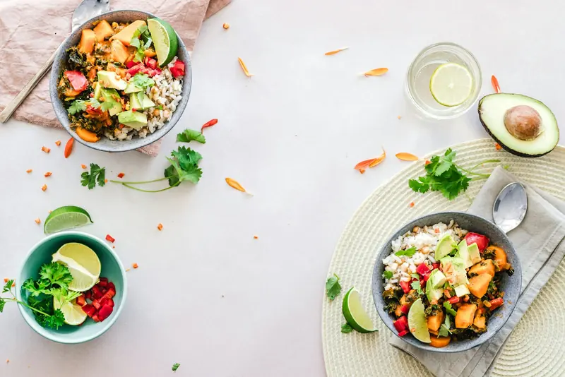 Bowls seen from above with rice, vegetables, avocado and lime on a white table