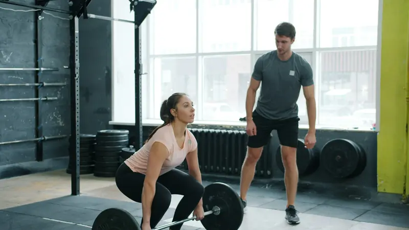Personal Trainer beaufsichtigt eine Frau, die im Fitnessstudio eine Langhantel hebt