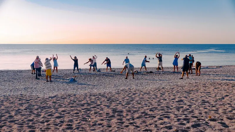 Gruppe von Erwachsenen trainiert bei Sonnenaufgang gemeinsam am Strand