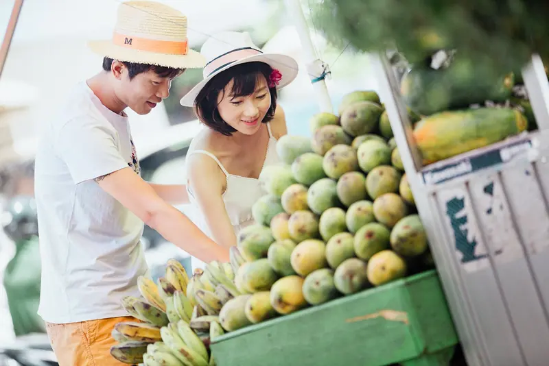 Pareja con sombreros eligiendo fruta tropical en un puesto de mercado