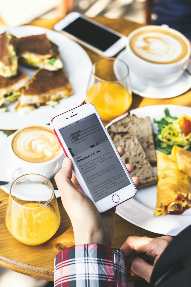 Hand holding a phone over a breakfast table with milky coffee and orange juice