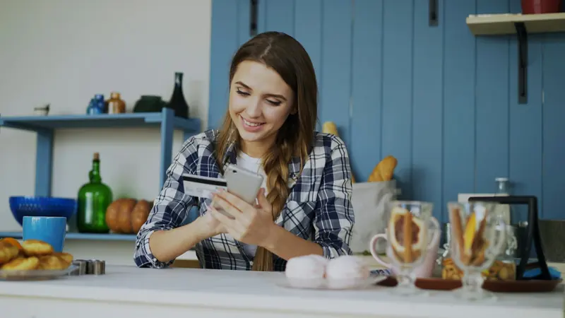 Smiling woman looking at her phone, sitting in a bright kitchen