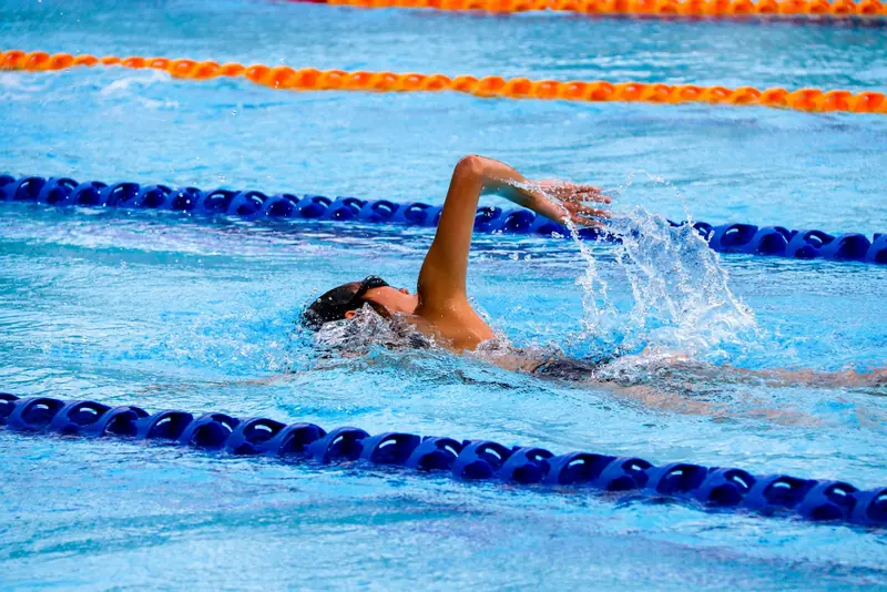 Persona nadando a crol en una piscina entre corcheras azules y naranjas