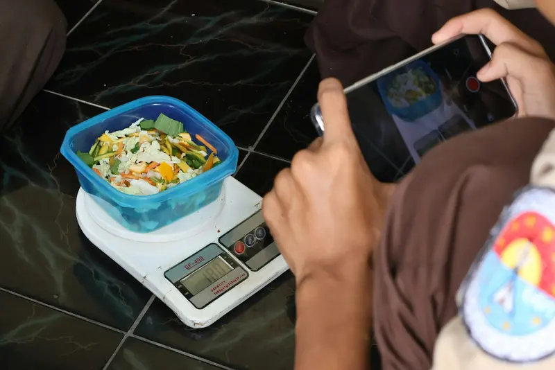 Bowl of chopped vegetables being weighed on a digital scale while being filmed with a phone