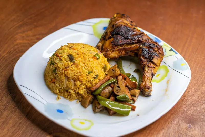 Plato con muslo de pollo asado, arroz amarillo y verduras salteadas